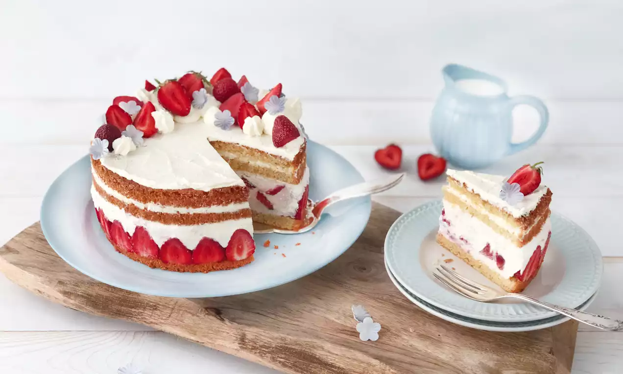 Kleine Erdbeer-Mascarpone-Torte mit Schichten aus hellem Biskuit und weißer Creme, dekoriert mit Erdbeerstücken und Sahnetupfen auf weißem Teller