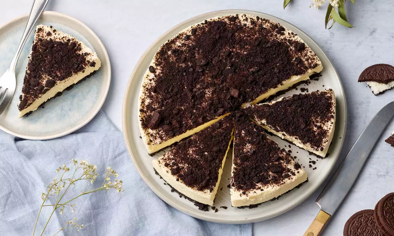 Oreotorte mit heller cremefarbener Füllung und dunklem Oreo-Keksbrösel-Topping, serviert auf einem Teller, daneben ein angeschnittenes Stück