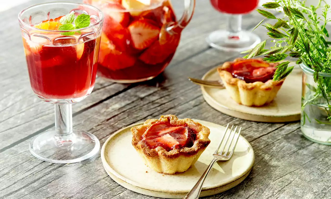 Mandelcremetærte med gylden kant og rød sangriagelé fyld, serveret på lys keramiktallerken med gaffel ved siden af