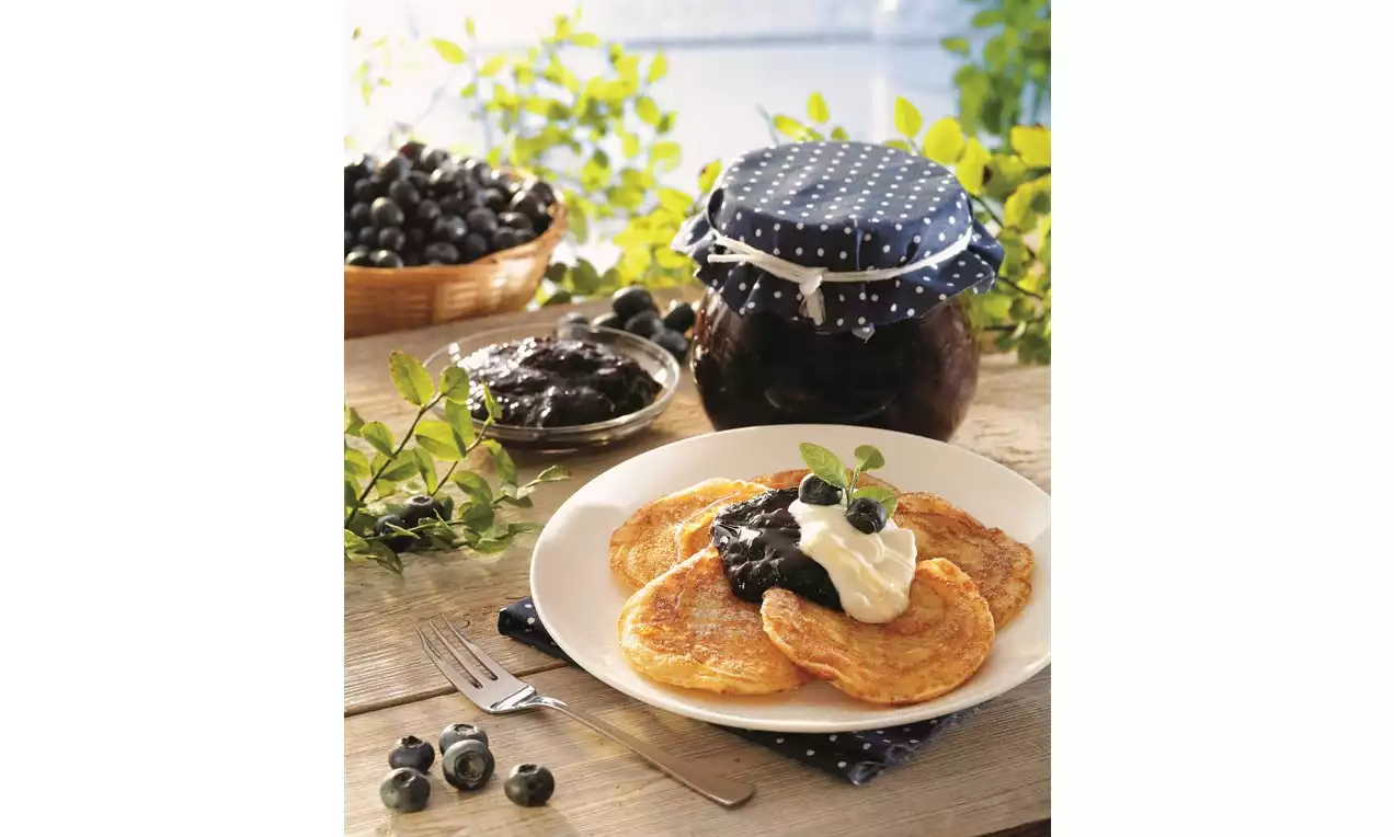 Na bielom tanieri sú zlatisté lievance zdobené kopčekom šľahačky, čučoriedkovým džemom a lístkom mäty, obklopené čerstvými čučoriedkami