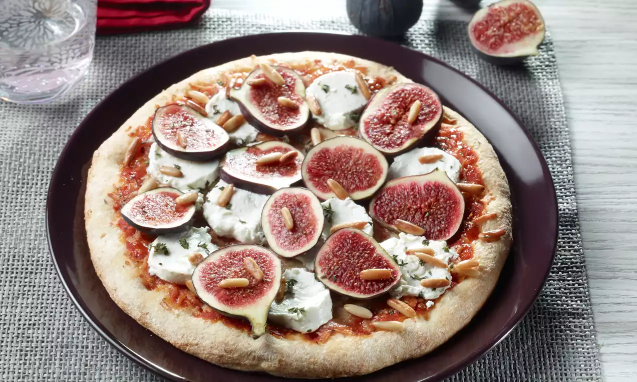 Runde Pizza mit goldbraunem Rand, belegt mit Ziegenkäse, frischen Feigen und Pinienkernen, auf einem dunkelbraunen Teller angerichtet