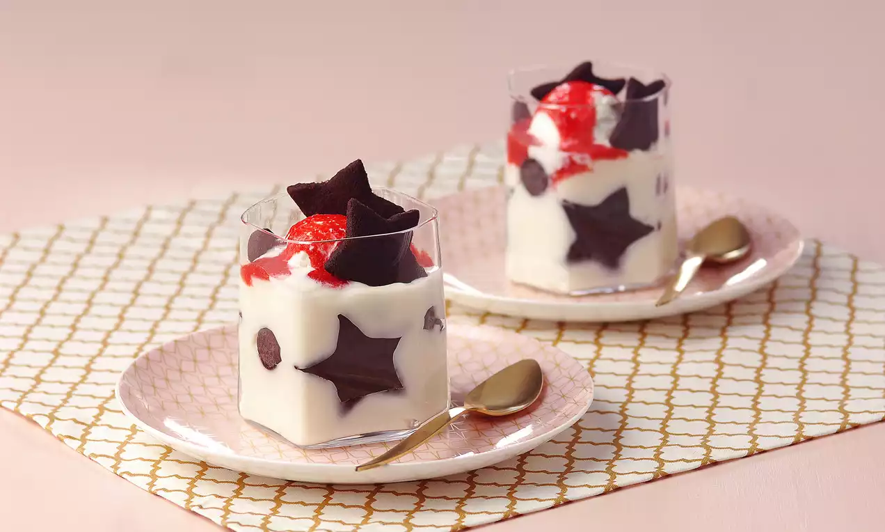 Sakızlı beyaz muhallebiyle dolu şeffaf kupalarda, yıldız şeklindeki çikolatalarla ve kırmızı soslu toplarla süslenmiş düzenleme