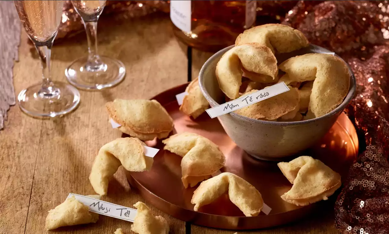 Zlatisté sušienky šťastia v tvare polmesiacov s jemne popraskaným povrchom, usporiadané v bielej miske a voľne položené na medenej tácke