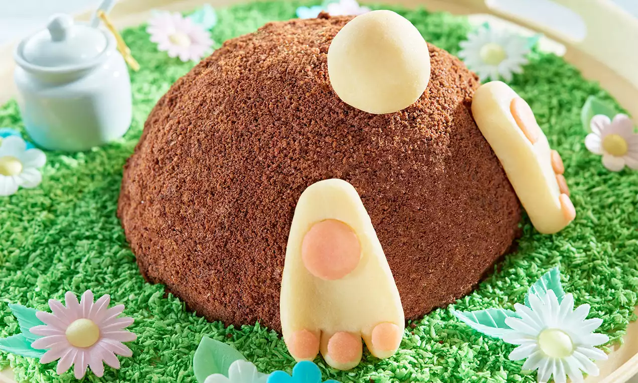 Kopcovitá torta s hnedou čokoládovou striedkou posadená na zelenej kokosovej tráve, ozdobená marcipánovými labkami a kvetmi.