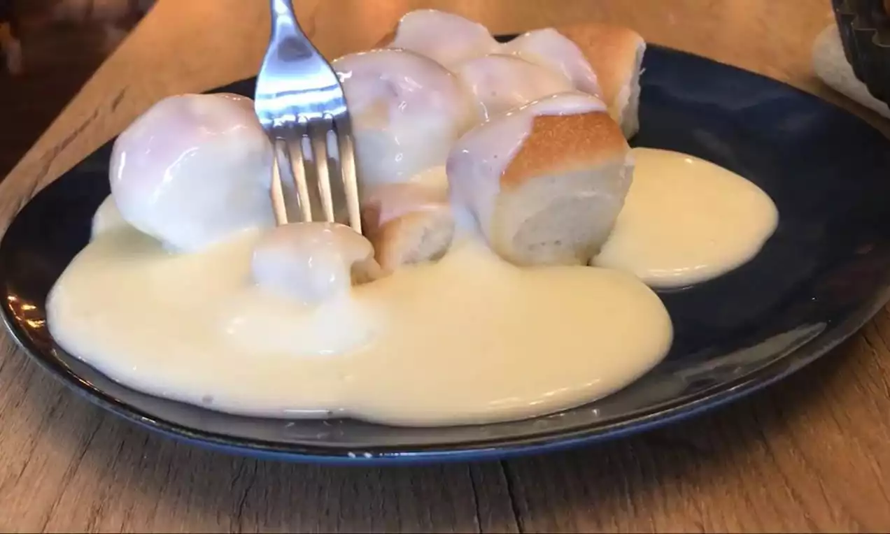 Malé, nadýchané svetlé buchtičky s jemne opečenou kôrkou na tmavomodrom tanieri, zaliate lesklým vanilkovým krémom, s vidličkou pripravenou k nakrojeniu