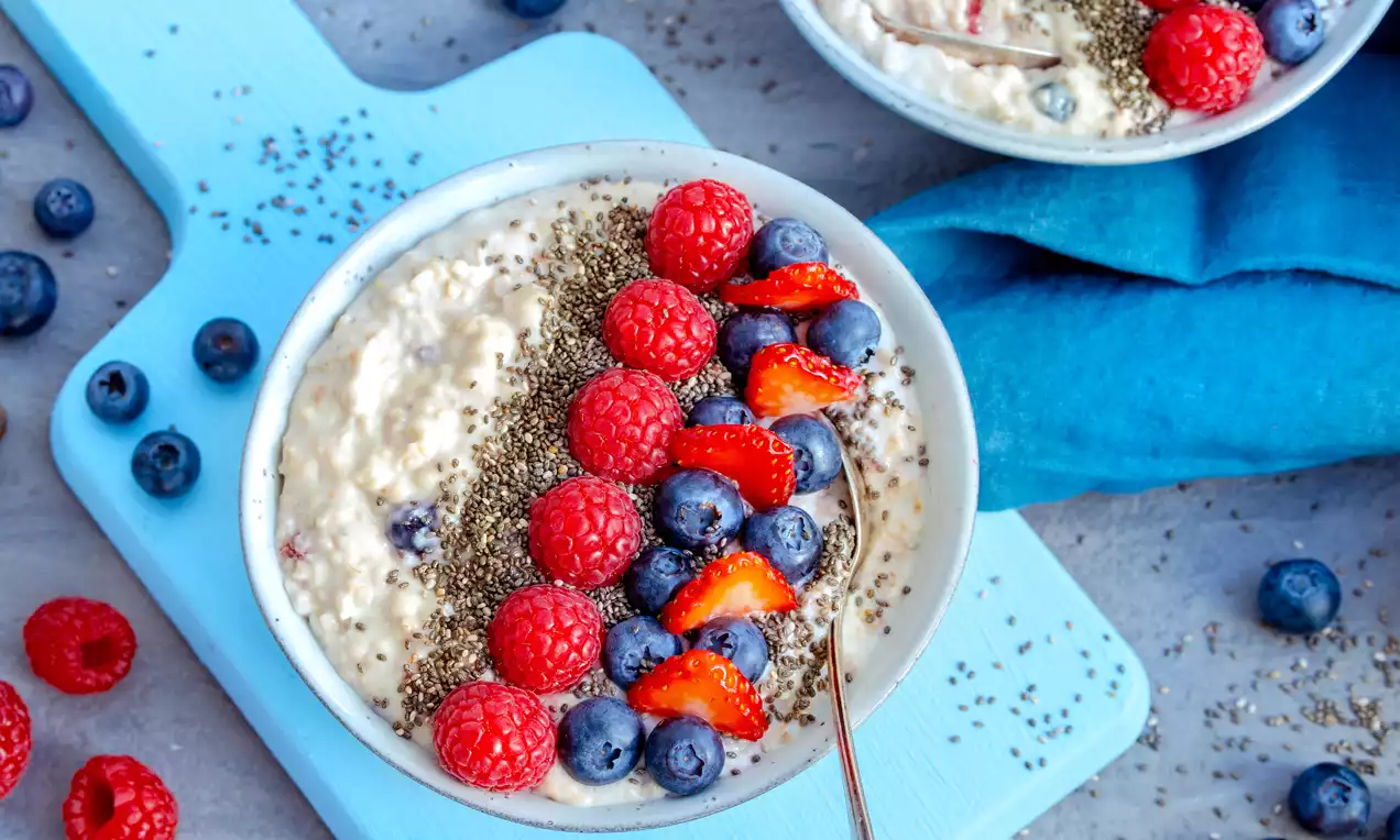 Cremiges beigees Porridge in einer hellen Schale, belegt mit frischen roten Himbeeren, blauen Blaubeeren, Erdbeerscheiben und Chiasamen
