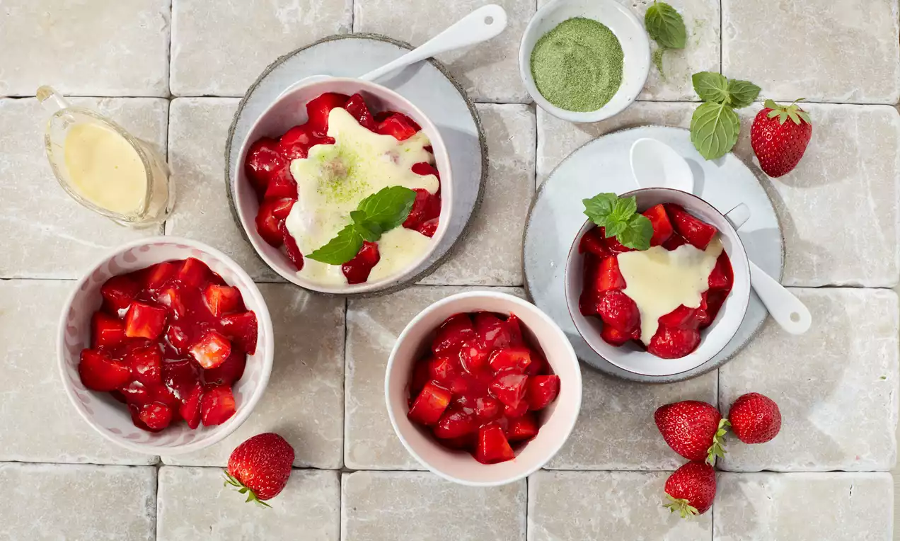 Erdbeergrütze in weißen Schalen, mit Vanillesauce und Minzblättern garniert, frische Erdbeeren und Matchapulver dekorativ arrangiert