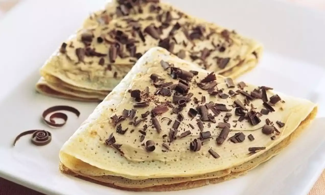 İnce katmanlı üçgen krepler üzerine açık kahverengi krema sürülmüş, sütlü çikolata parçalarıyla süslenmiş, beyaz bir tabakta sunulmuş