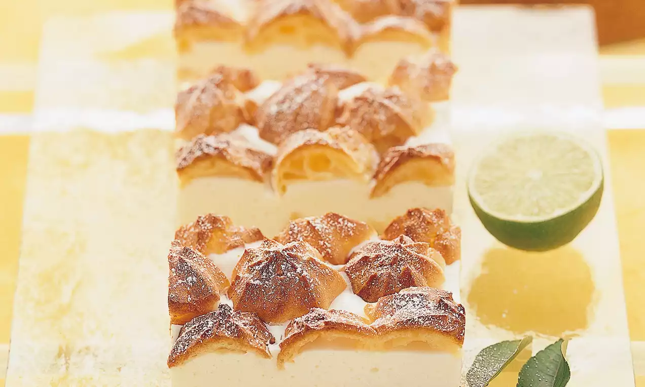 Limettis mit goldbrauner Baiserhaube auf cremiger Füllung, angerichtet auf einer Glasplatte, umgeben von frischen Limetten und Blättern