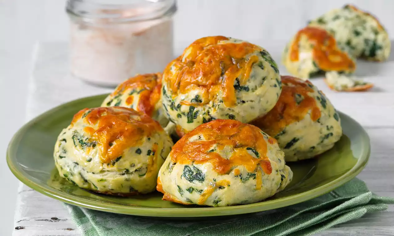 Špenátové koláčiky zlatisto zapečené, guľaté a jemne porézne, posiate kúskami špenátu, na zelenom tanieri s ľanovým obrúskom