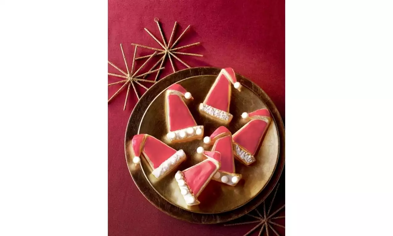 Perníčky ve tvaru červených santovských čepic s cukrovou polevou, bílé detaily a perličky na zlatém talíři, obklopené hvězdicovou dekorací