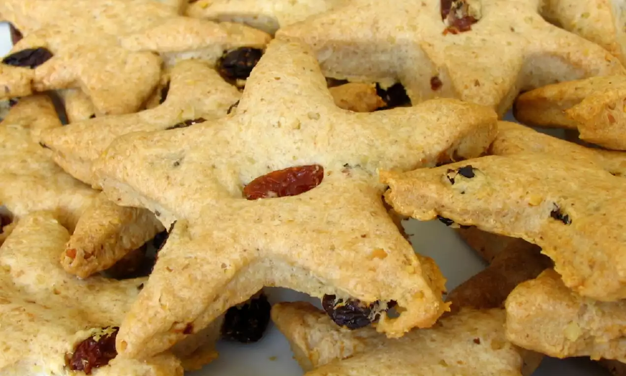 Altın rengi ve kıtır dokulu, yıldız şekilli kurabiyeler, yüzeylerinde bütün kuru üzümlerle bir arada tabakta düzenlenmiş.