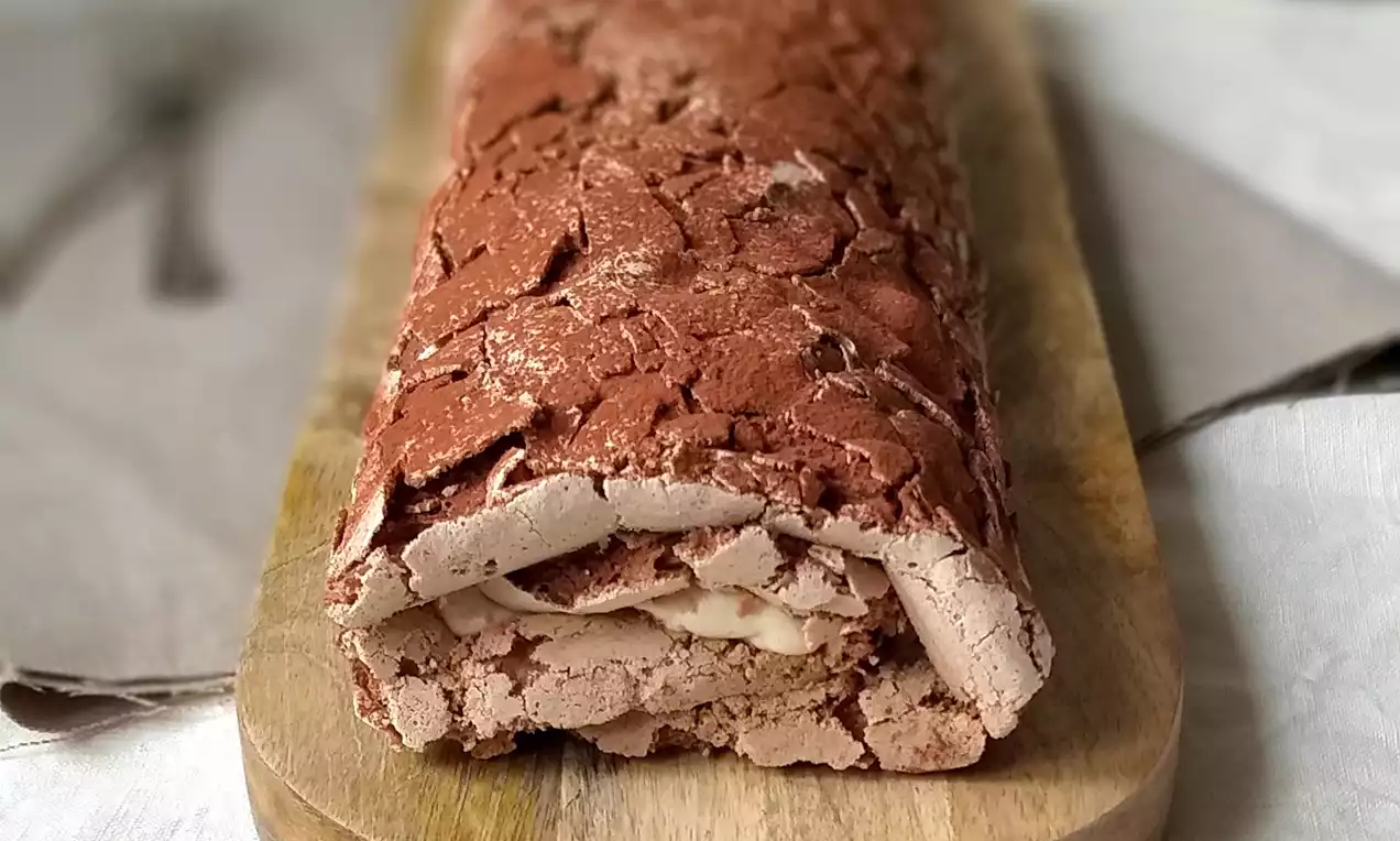 Bílková kávová roláda čokoládovej farby s popraskanou textúrou na povrchu, plnená svetlým krémom, podávaná na drevenom podnose