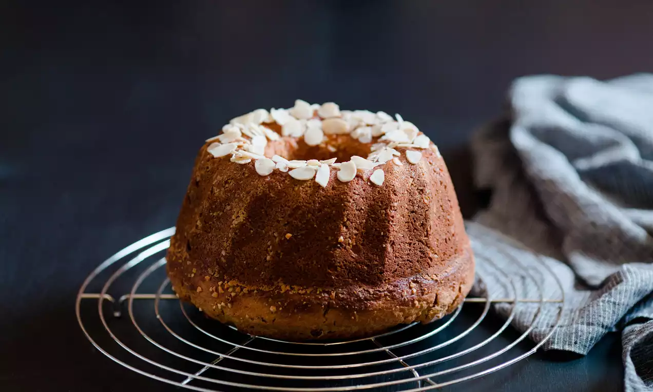 Koyu altın rengi ve yüksek halkalı şekliyle kabuk kısmı gevrek, üzeri file bademlerle süslenmiş kek, tel ızgara üzerinde