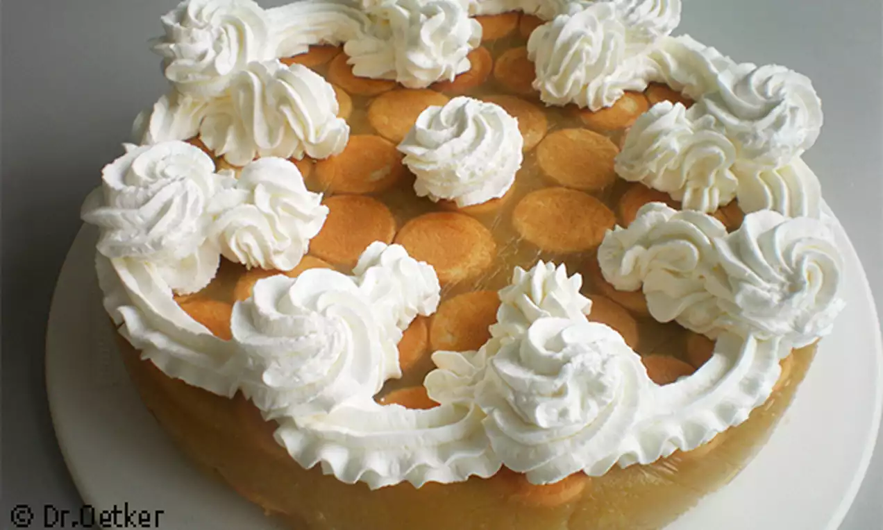 Svetložltý jablkový základ so zaoblenými okrajmi, hladkou textúrou, pokrytý vrstvou piškót a zdobený kopčekmi šľahačky do kruhu