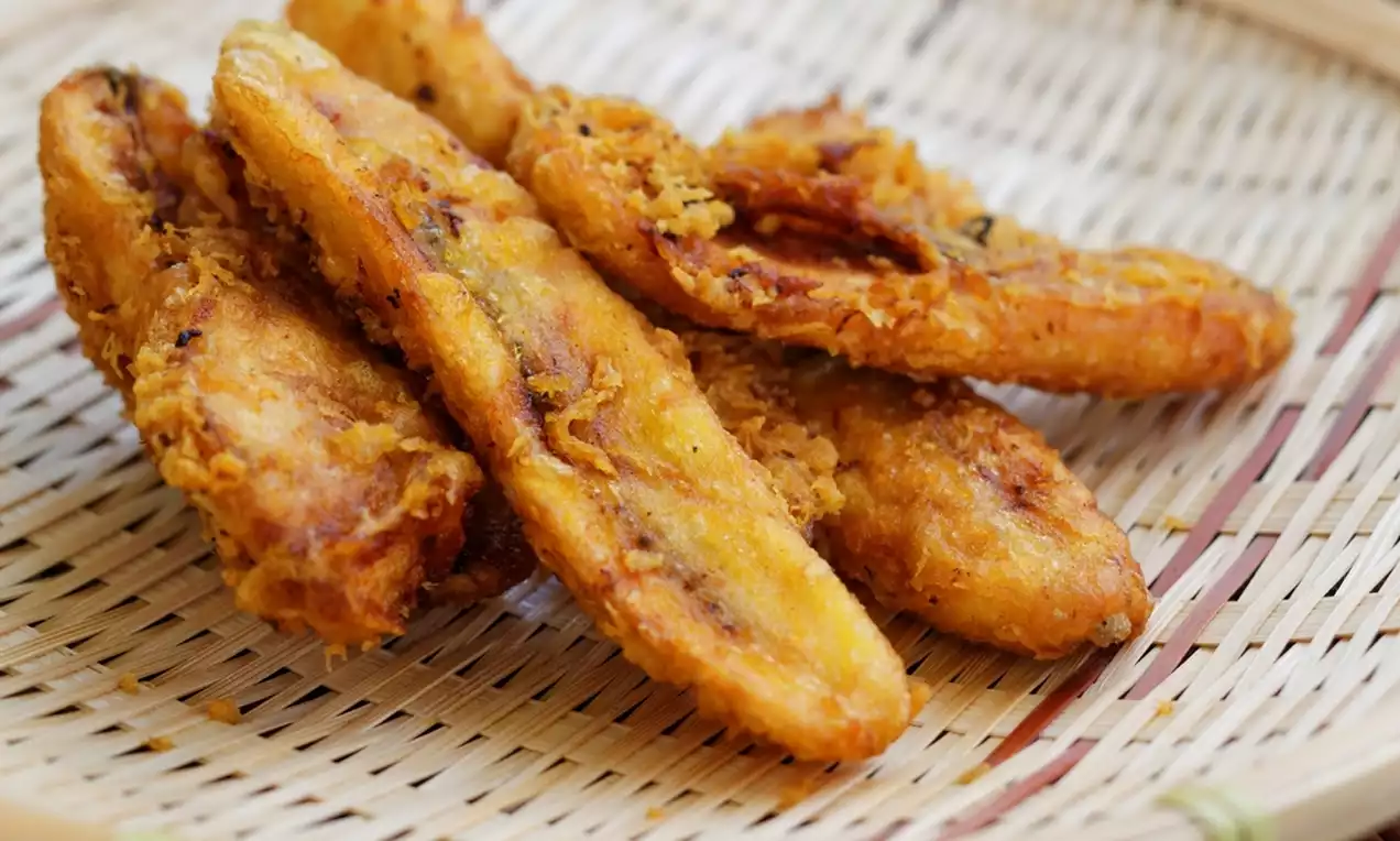 Golden, crispy-fried banana slices with jagged edges and a flaky texture, arranged in a pile on a woven bamboo tray