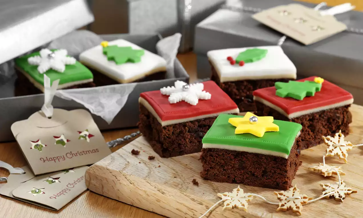 Square chocolate brownies topped with smooth red, green, or white icing, decorated with festive shapes on a wooden board