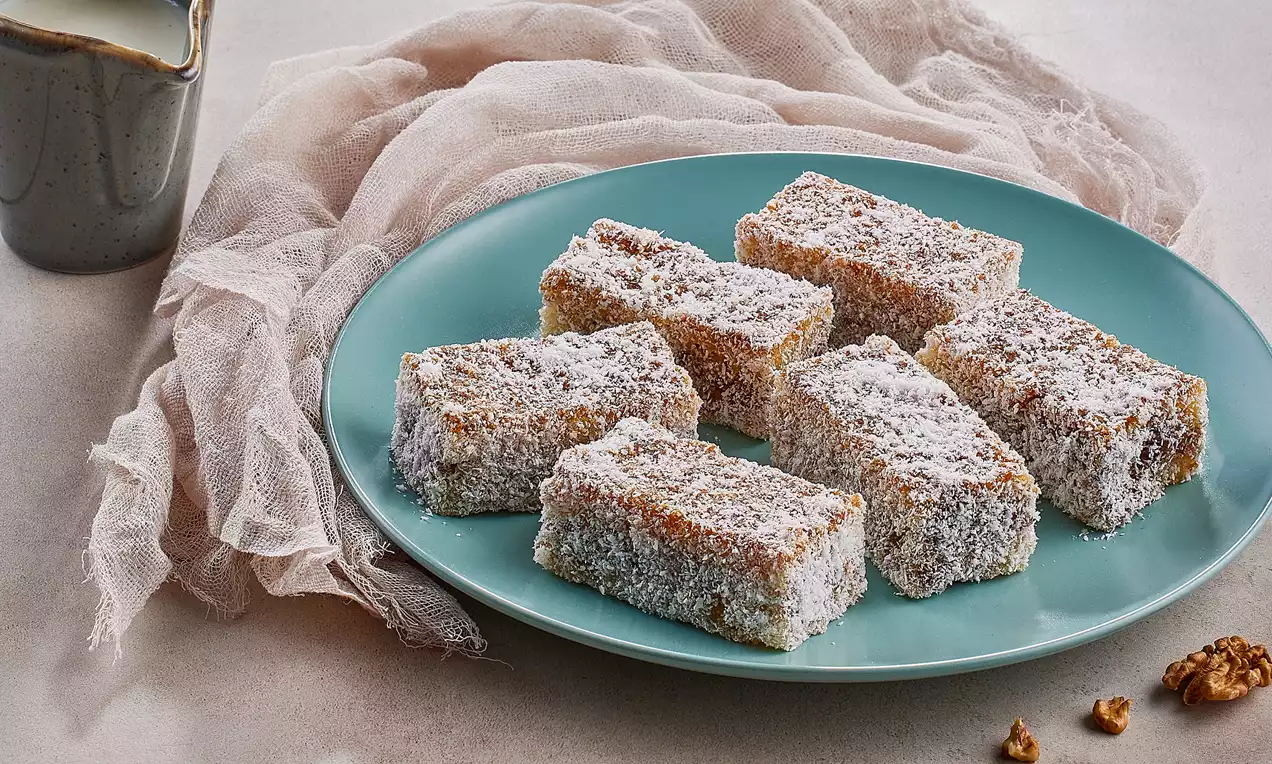 Dikdörtgen kesilmiş, üzeri yoğun pudra şekeriyle kaplı Halep tatlısı, açık mavi bir tabakta düzgün sıralanmış şekilde sunulmuş