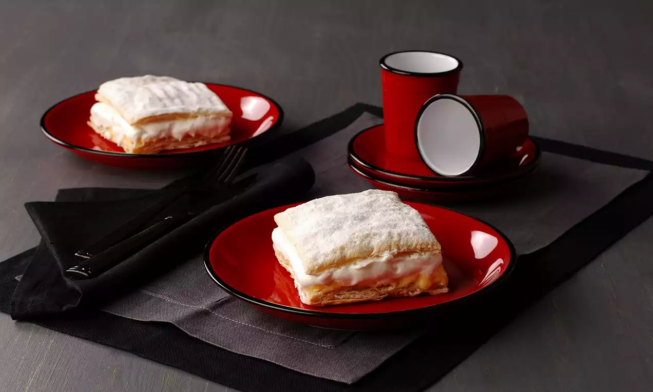 Kat kat çıtır hamur arasında kremayla dolu, üzeri pudra şekeri serpilmiş kremsniteler kırmızı tabaklarda siyah peçete üzerinde sergileniyor