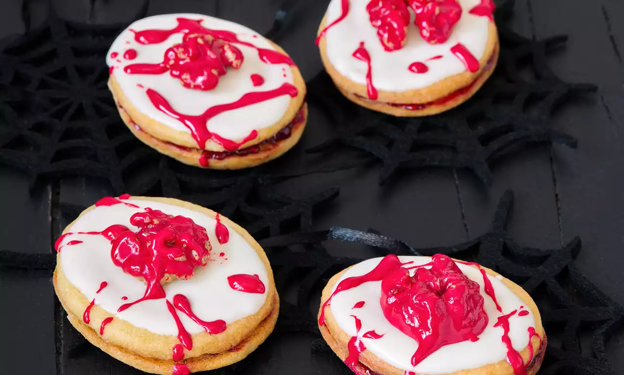 Oválné máslové sušenky spojené marmeládou, pokryté bílou polevou s červenými krémovými vzory připomínajícími mozky na černém podkladu