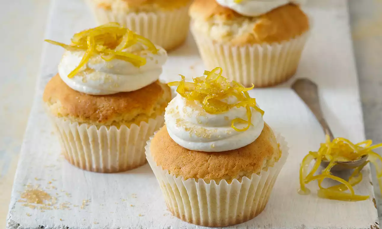 Cupcakes ve světlém papírovém košíčku, se svěží citronovou kůrou na nadýchaném krému, uspořádané na bílé dřevěné desce