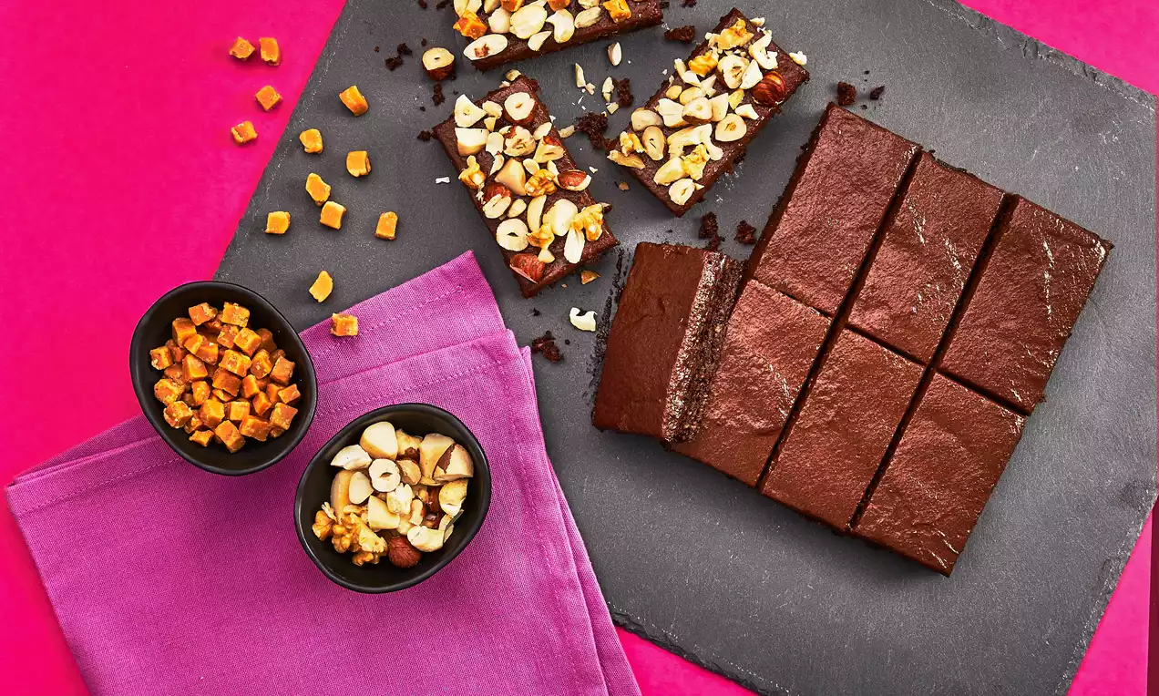 Suklaanruskeat, tasaiset brownie-palat aseteltuina mustalle liuskekivialustalle, viereen ripoteltu pähkinöitä ja kuutioitua hedelmää