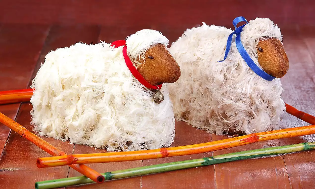 Tüy gibi ince dokulu beyaz görünümde, kırmızı ve mavi kurdelelerle süslenmiş iki kuzu figürü renkli çıtalarla çevrili kompozisyonda