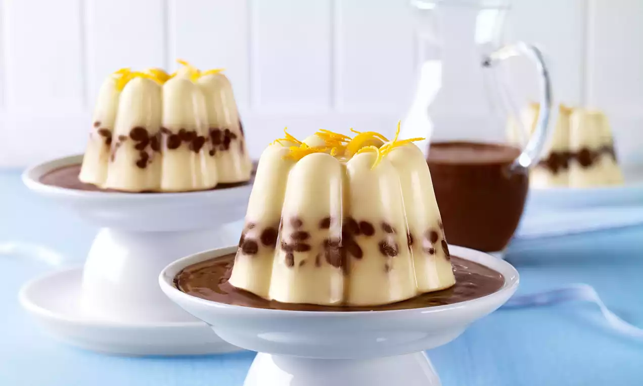 Vanillefarbiger Pudding mit Schokotropfen in Gugelhupfform, garniert mit Zitronenzesten, serviert auf Schokosoße auf weißer Dessertschale
