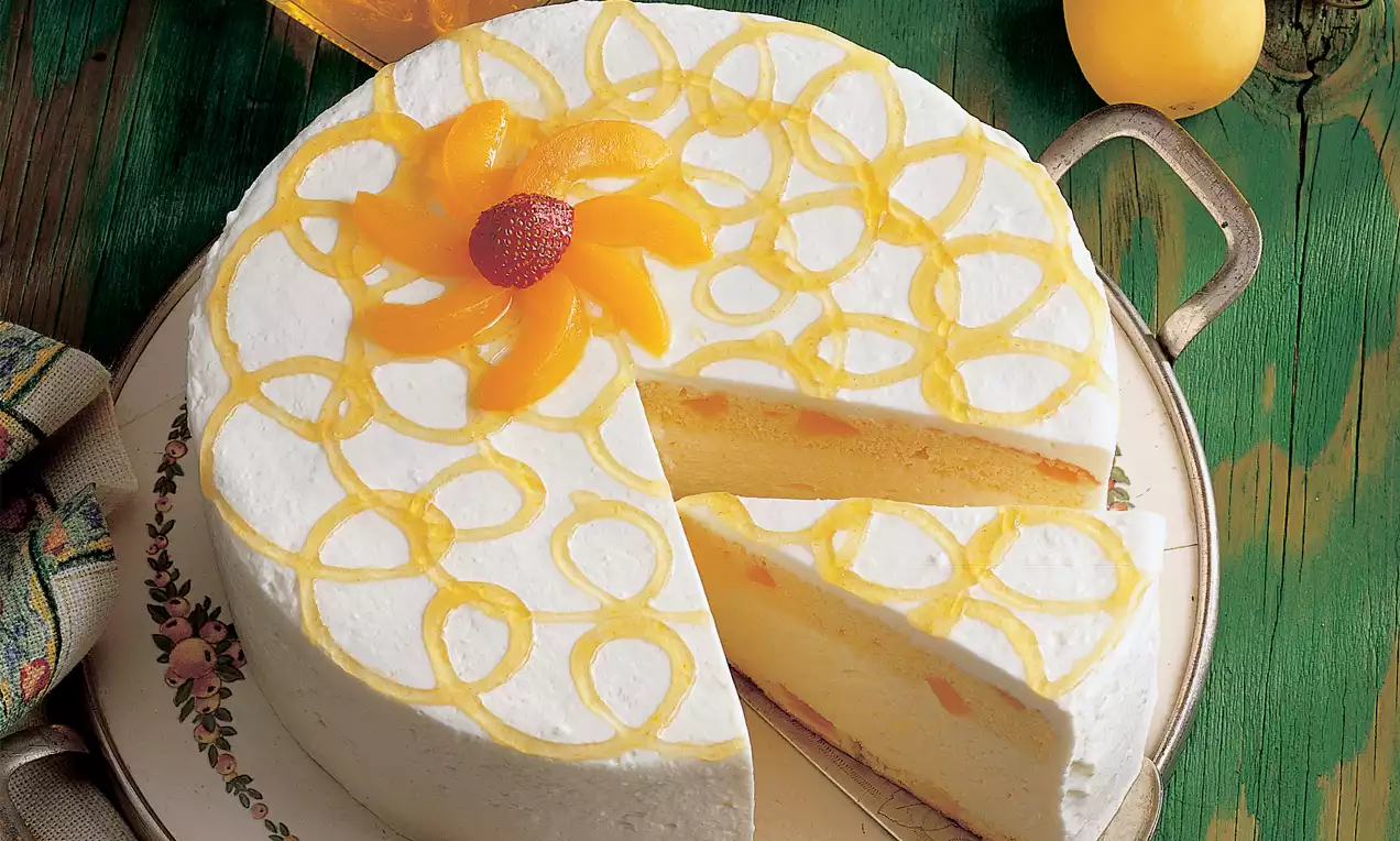 Mariandltorte mit weißer Sahnehaube, gelbem Pfirsichmuster und dekorativer Blüte, angeschnitten auf einem Porzellanteller mit floralem Rand