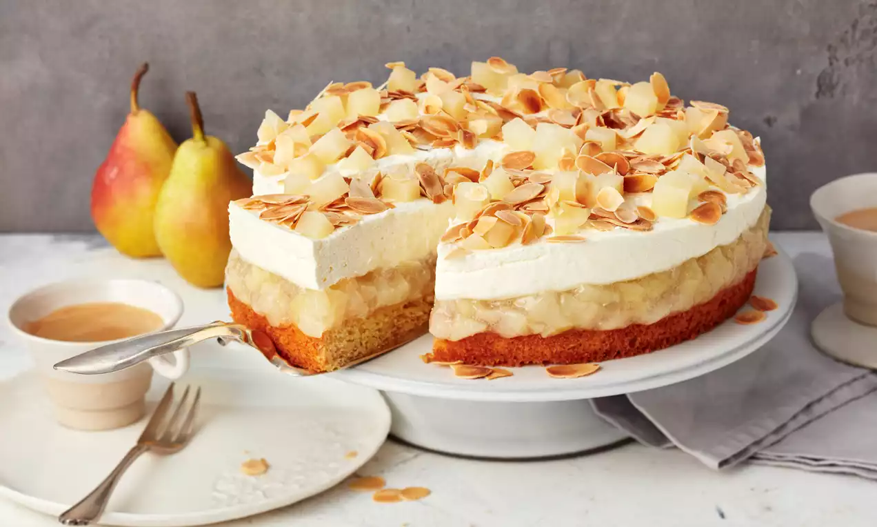 Birnentorte mit fluffiger Sahneschicht, goldbraunem Boden und karamellisierten Mandelblättchen auf weißer Tortenplatte angerichtet