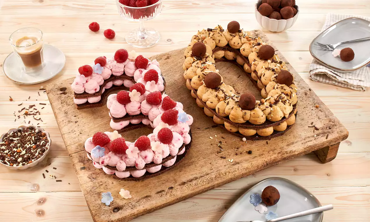 Zahlentorte mit rosa Himbeer-Mascarpone, dunkler Schoko-Karamell-Creme, frischen Himbeeren und goldenen Streuseln auf Teller