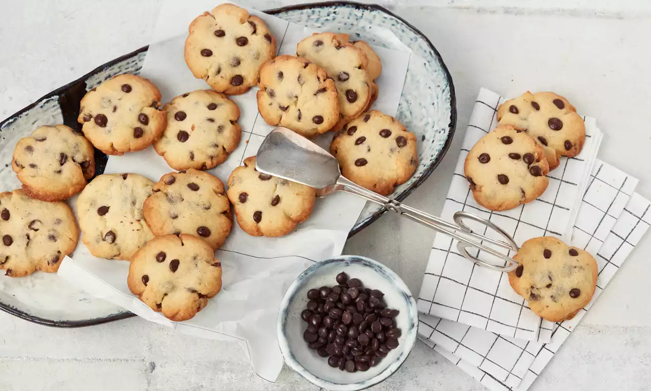 Goldbraune Chocolate-Chip-Cookies mit dunklen Schokoladenstückchen auf weißem Backpapier in einer ovalen Keramikschale angerichtet