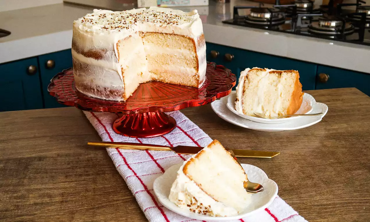 Bolo 4 leites com cobertura cremosa branca, fatias mostrando miolo úmido e calda levemente dourada escorrendo, servido em prato