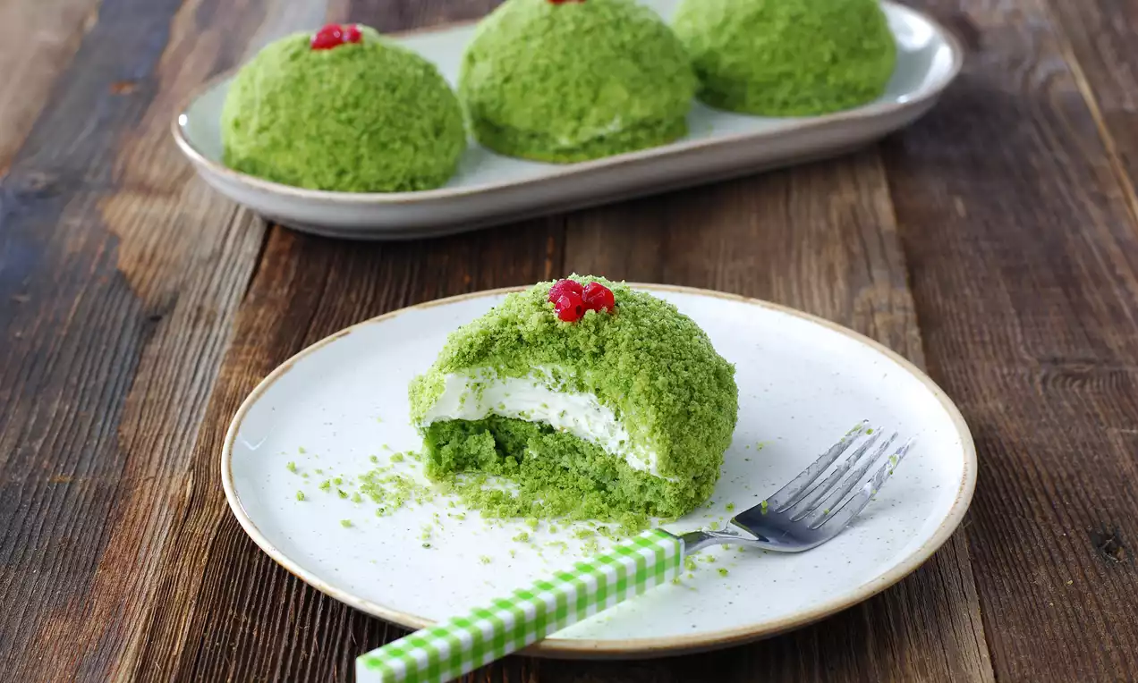 Yuvarlak formda ispanağın canlı yeşil tonlarında kaplanmış pastacıklar, kremalı dolgu ile katmanlı ve kırmızı meyveyle süslenmiş