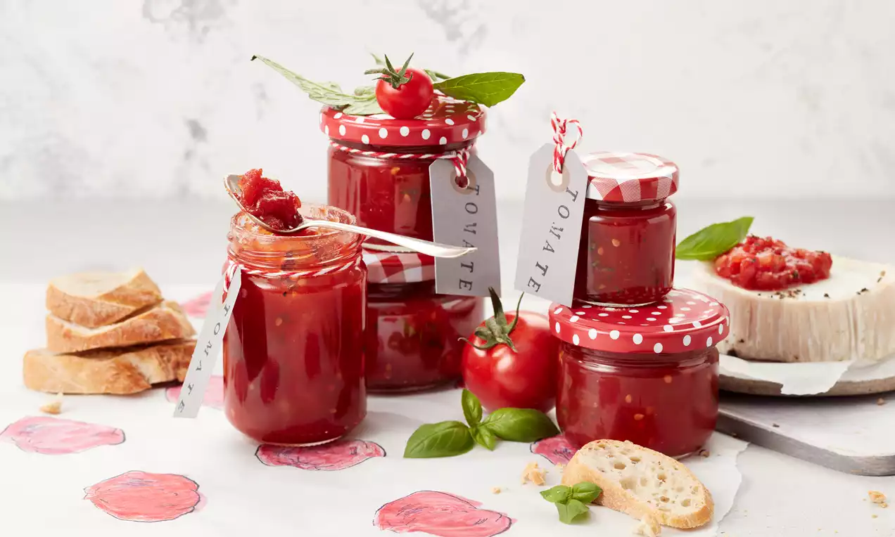 Eingekochte Tomaten in Bügelgläsern: leuchtend rote, ganze und stückige Tomaten mit Olivenöl, Basilikumblättern und Knoblauch auf Holzbrett