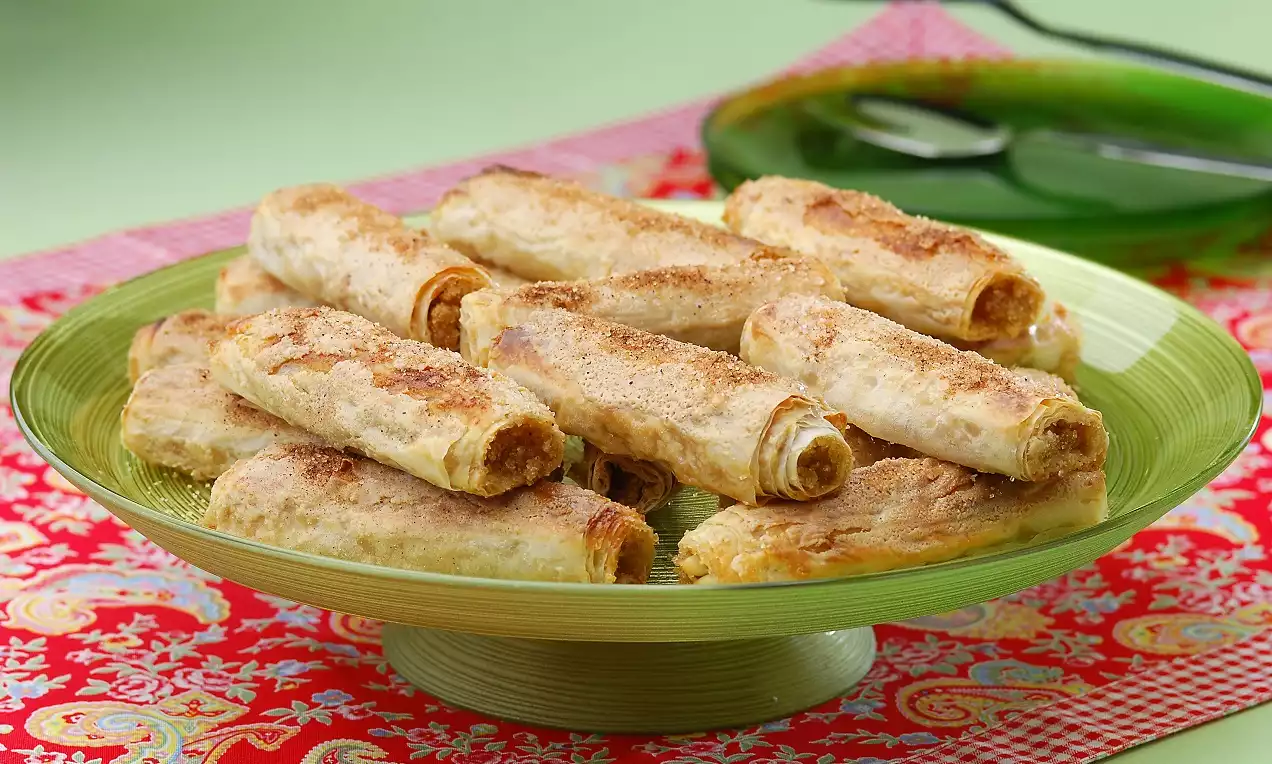 İnce ve altın renginde çıtır rulolar, yeşil cam tabakta düzenli bir şekilde dizilmiş, kırmızı desenli örtü üzerinde sunulmuş