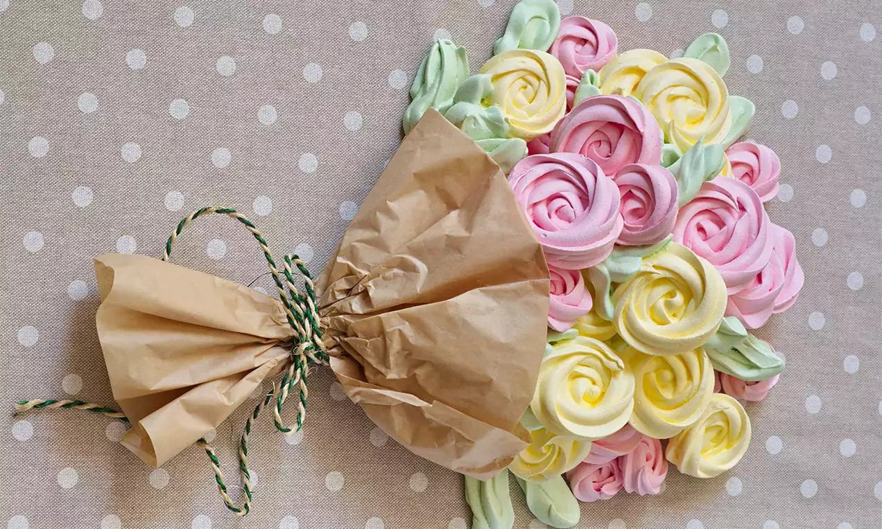 Květy z růžové, žluté a zelené cukrové pěny uspořádané do kytice, zavázané provázkem v hnědém papíru na puntíkovaném podkladu