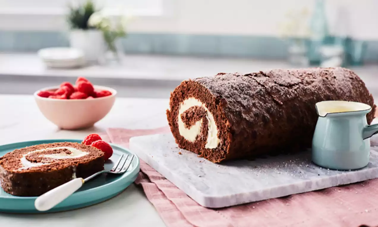 Chocolate Swiss roll with a rich cocoa sponge rolled around a white cream filling, served on a marble board with raspberries and cream nearby