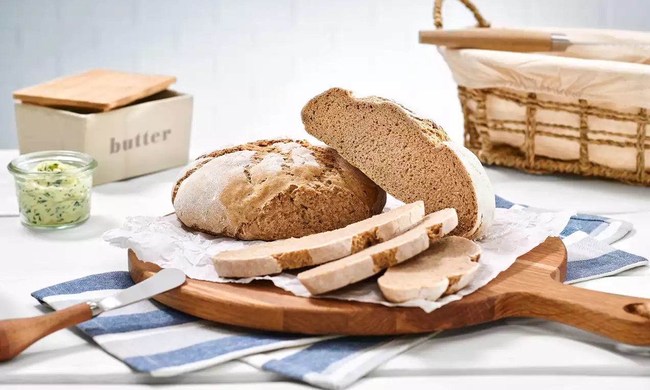 Rundes Sauerteigbrot mit hellbrauner Kruste und weicher Krume, in Scheiben geschnitten auf Holzbrett mit gestreiftem Tuch angerichtet