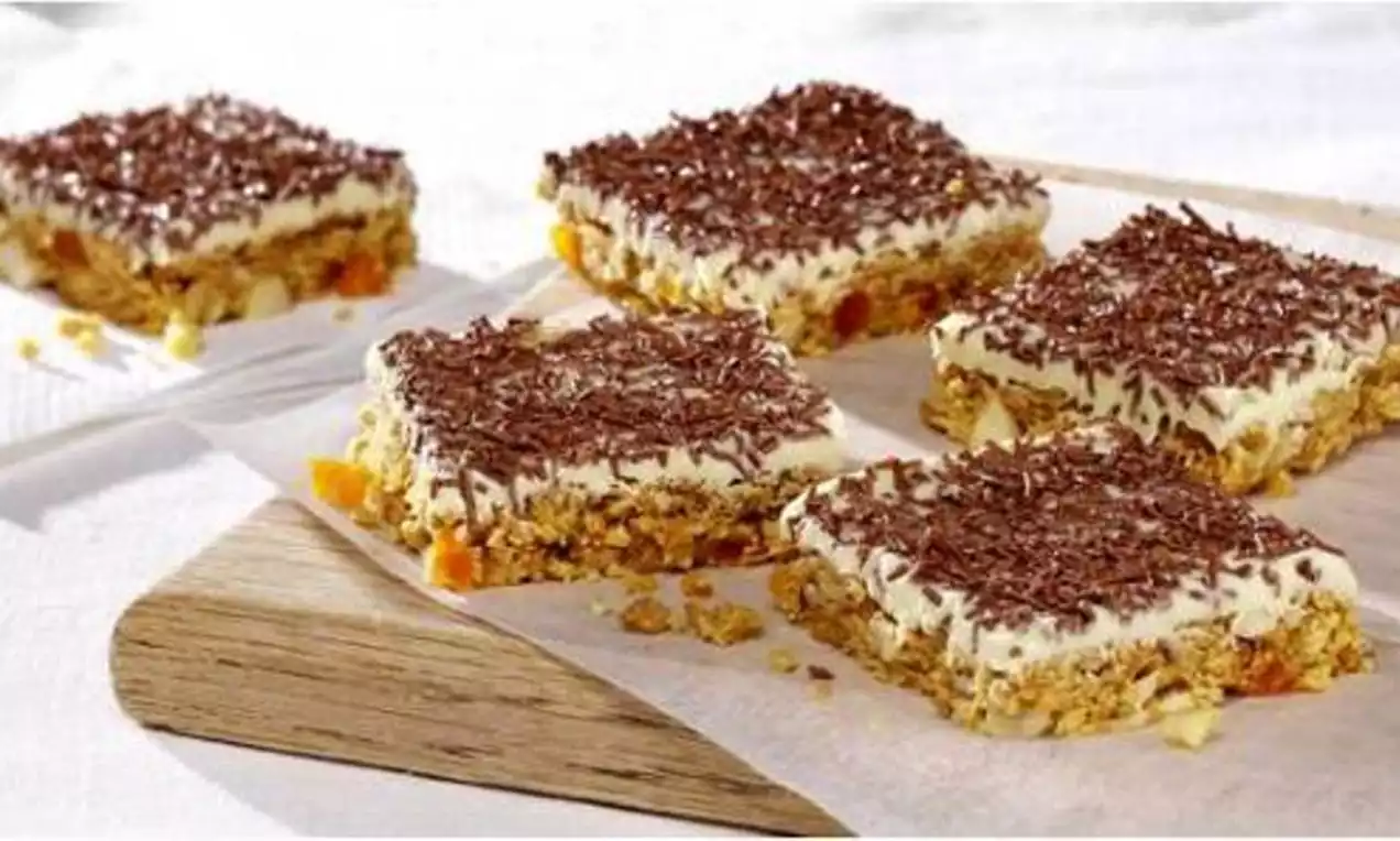 Square slices of white chocolate tiffin with a golden crumb base, creamy pale topping and dark chocolate shavings on parchment paper