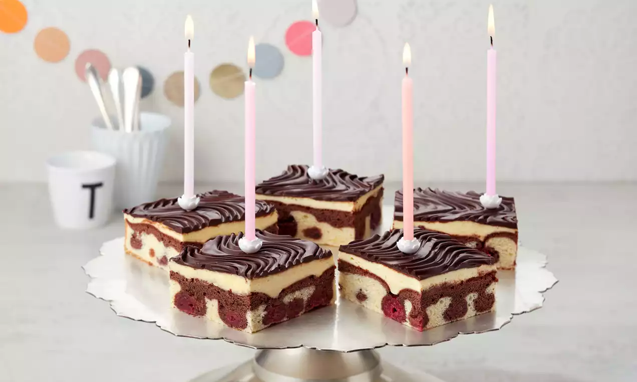 Schneewittchen-Kuchen mit heller Creme, dunklem Schokoladenguss und Kirschen auf einer silbernen Platte mit fünf rosa und weißen Kerzen