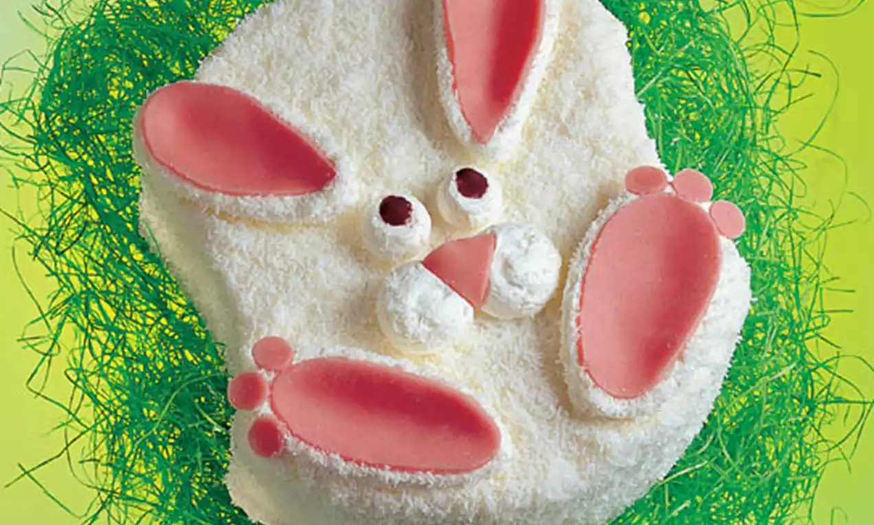 Gâteau en forme de lapin avec une texture blanche moelleuse, oreilles et pattes roses en sucre cernées de pailles vertes sur fond jaune