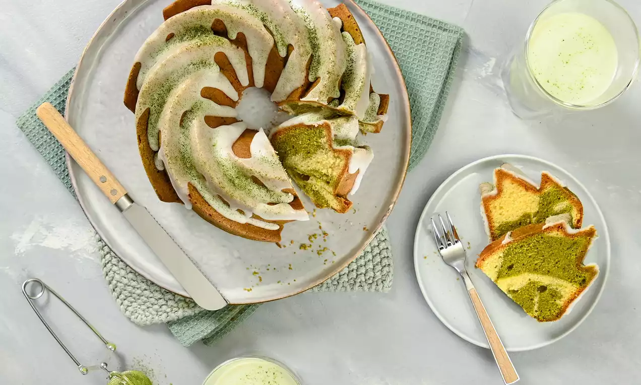 Vegan bábovka ve tvaru kruhové spirály, dvoubarevné vrstvy zelené a světlé hnědé, zdobená bílou polevou a zeleným práškem na keramickém talíři