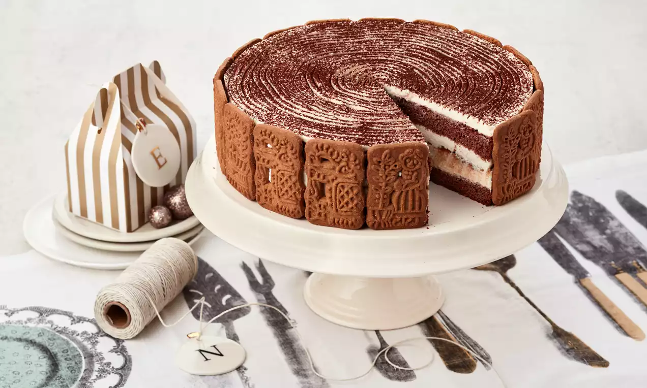 Spekulatius-Tiramisu-Torte mit braunen Spekulatiuskeksen am Rand, cremeweißen Schichten und Kakao auf dem Topping, serviert auf weißer Tortenplatte