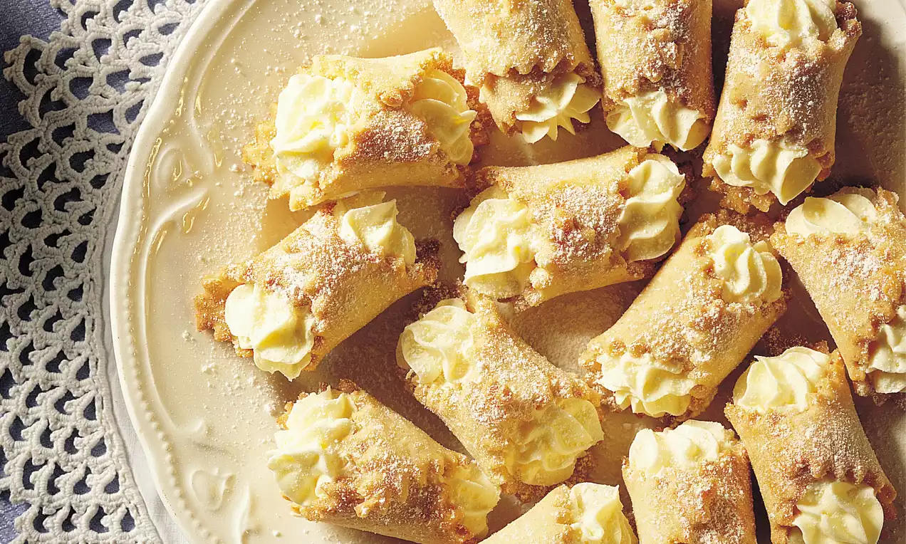 Knusprige, goldbraune Teigrollen mit gezackten Rändern, gefüllt mit hellgelber Creme und bestäubt mit feinem Zucker auf einem weißen Teller