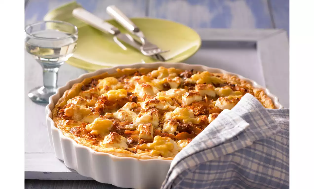 Goldbraune Weißkohl-Blätterteig-Quiche mit blättriger Kruste in weißer Tarteform, daneben kariertes Küchentuch und gedeckter Tisch