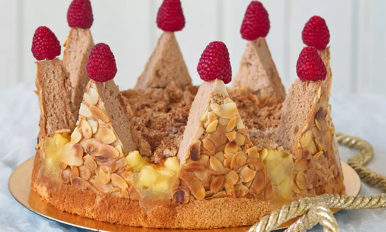 Krémová torta s jemne hnedými mandľovými lupienkami, zahrotenými vežami zo svetlohnedého cesta, ozdobená červenými malinami na zlatom podnose