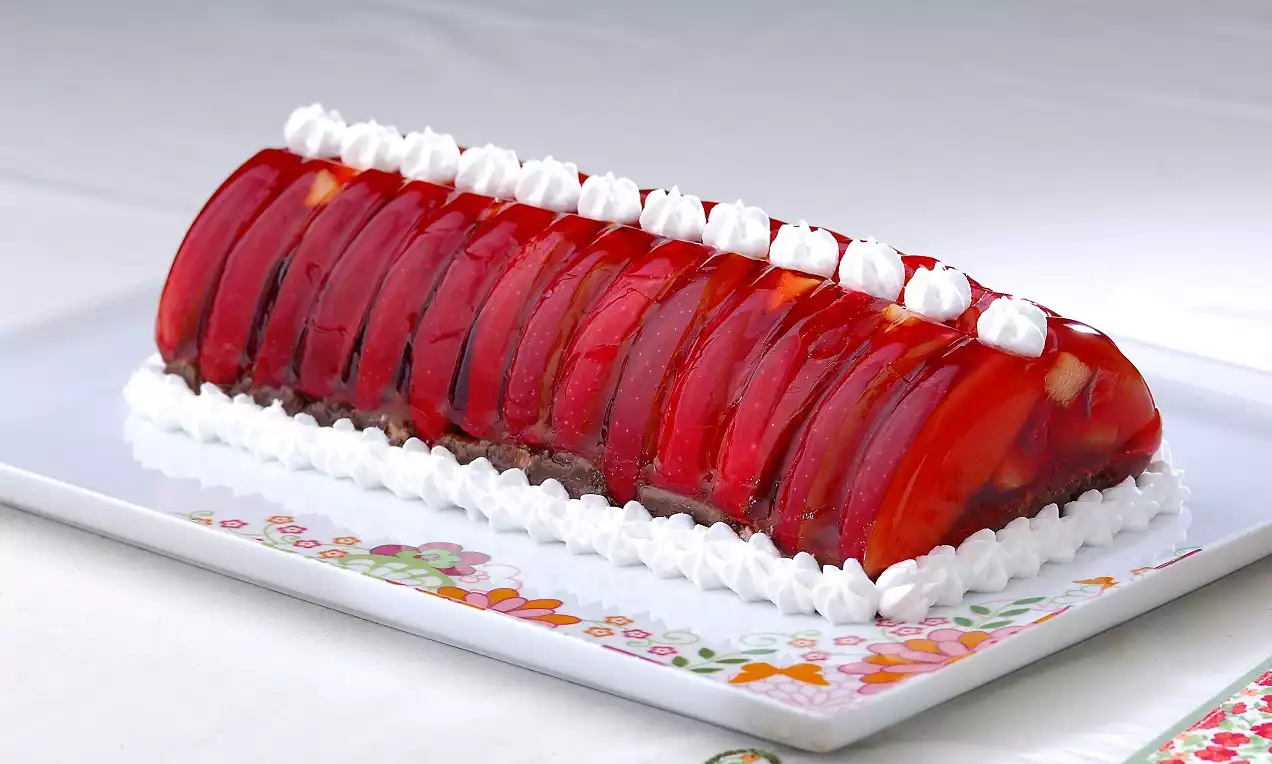 Parlak kırmızı jöle dilimleriyle süslenmiş dikdörtgen pasta, beyaz krem şanti bordürleri ve renkli desenli tabakta sunulmuş