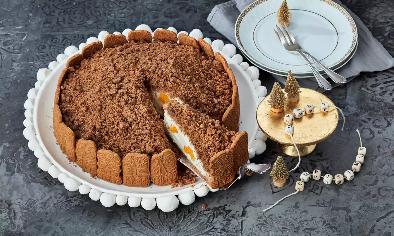 Kuchen mit Krümel-Schokoladenhaube, weißer Sahnefüllung und Mandarinenstücken, umgeben von Spekulatius auf weißer Keramikplatte