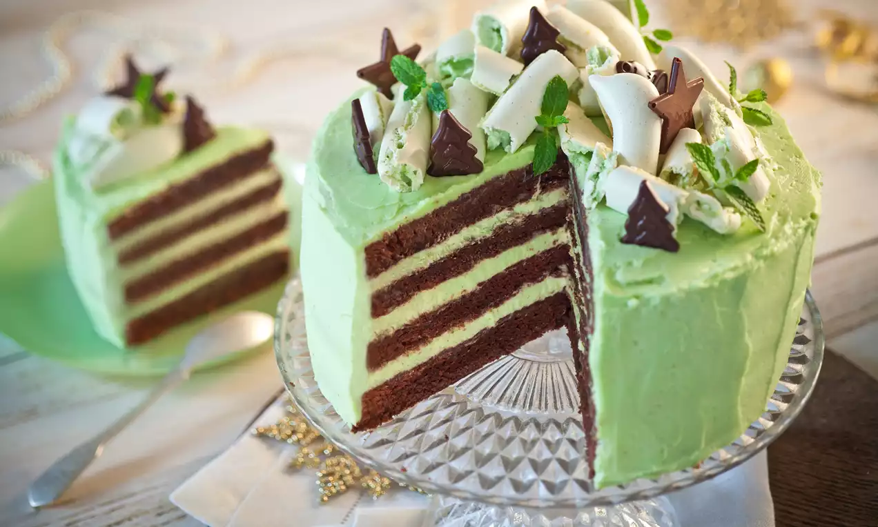 Tort czekoladowo-miętowy z warstwami ciemnego biszkoptu i miętowego kremu, udekorowany miętą, białymi rulonikami i czekoladowymi gwiazdkami